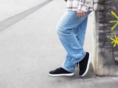 Eine Person in Jeans und Turnschuhen lehnt an einer mit Graffiti bedeckten Wand auf einem Bürgersteig.