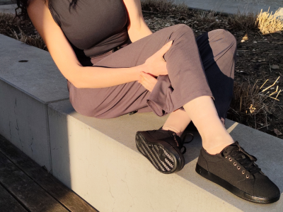 Eine Person in einem schwarzen Oberteil, einer grauen Hose und schwarzen Turnschuhen sitzt im Sonnenlicht auf einer Betonbank.