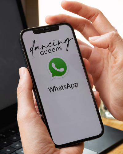 Person, die ein Smartphone hält, auf dessen Bildschirm das WhatsApp-Logo und der Text „Dancing Queens“ angezeigt werden.