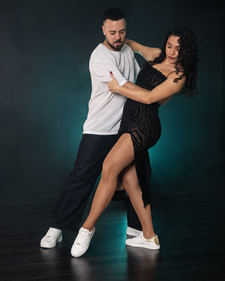 Tanzpaar in weissen Dance Sneakers in Tanzpose, dunkler Hintergrund mit türkisem Licht