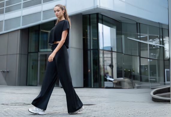 Frau in schwarzem Outfit geht an modernem Glasgebäude vorbei.