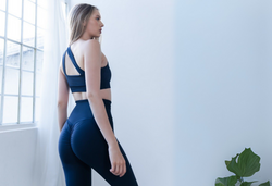 Eine Person in blauer Sportkleidung steht neben einem großen Fenster, auf der rechten Seite steht eine Pflanze.