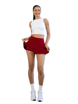 Frau in weißem Crop Top und Lismina 484 Rock in Bordeaux lächelt, steht und hebt eine Seite ihres Skorts.
