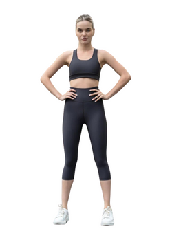 Person trägt Lismina 944 Capri-Leggings in Antrazit und Turnschuhe und steht selbstbewusst mit den Händen in den Hüften vor einem weißen Hintergrund.
