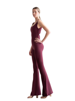 Frau in Lisminas dunkelviolettem Scrunch-Butt-Jumpsuit und Heels, steht im Profil vor einem weißen Hintergrund.