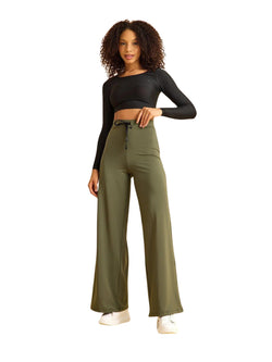 Frau in schwarzem bauchfreiem Top, Lismina 450 Mumbai Yoga Hose in Khaki, Hand auf der Hüfte, trägt weiße Turnschuhe.