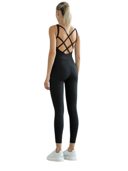 Seitlich stehende Person im Lismina 2100 Double Cross Jumpsuit in Schwarz mit weißen Sneakers und Pferdeschwanz.