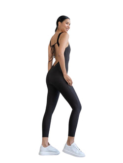 Frau in einem 1600 Full Body Jumpsuit von Lismina und weißen Turnschuhen, seitlich posierend und lächelnd vor einem weißen Hintergrund.