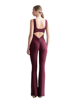 Eine Frau, die einen Lismina 1501 Scrunch Butt Jumpsuit in Dunkelviolett trägt, steht vor einem weißen Hintergrund.