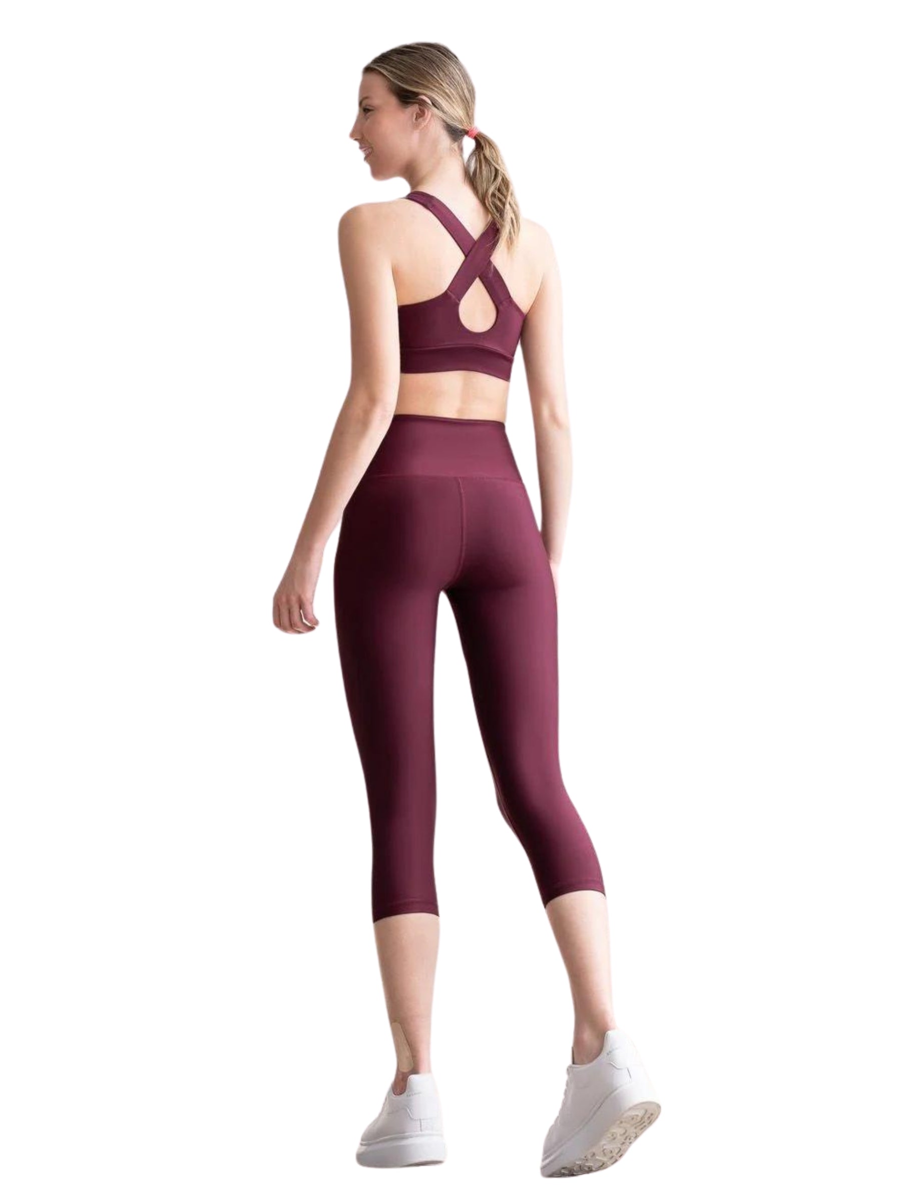 Frau in Lisminas Bordeaux 4312 Capri-Leggings und Cross-Back-Top, mit abgewandtem Gesicht, trägt weiße Turnschuhe.