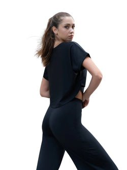 Person, die ein Lismina 100 Yoga T-Shirt in Schwarz trägt und auf einem weißen Hintergrund über die Schulter zurückblickt.