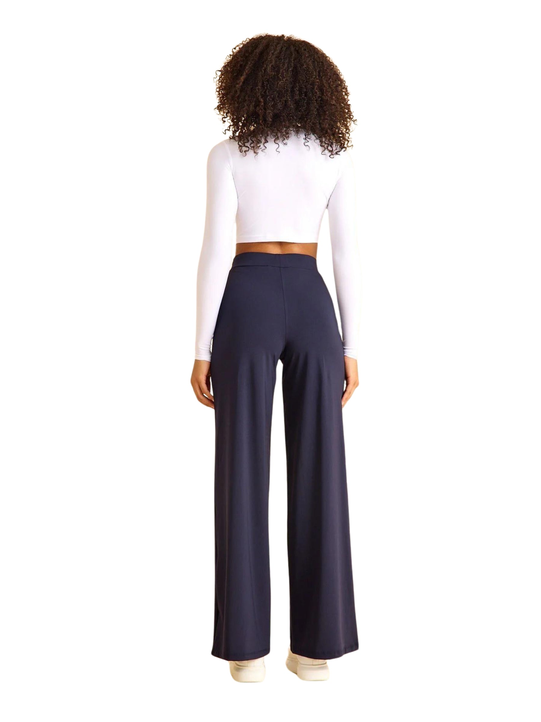 Eine lockige Frau in einem weißen bauchfreien Top und Lisminas 447 Mumbai Yoga Hose in Navy Blau, von hinten gesehen.
