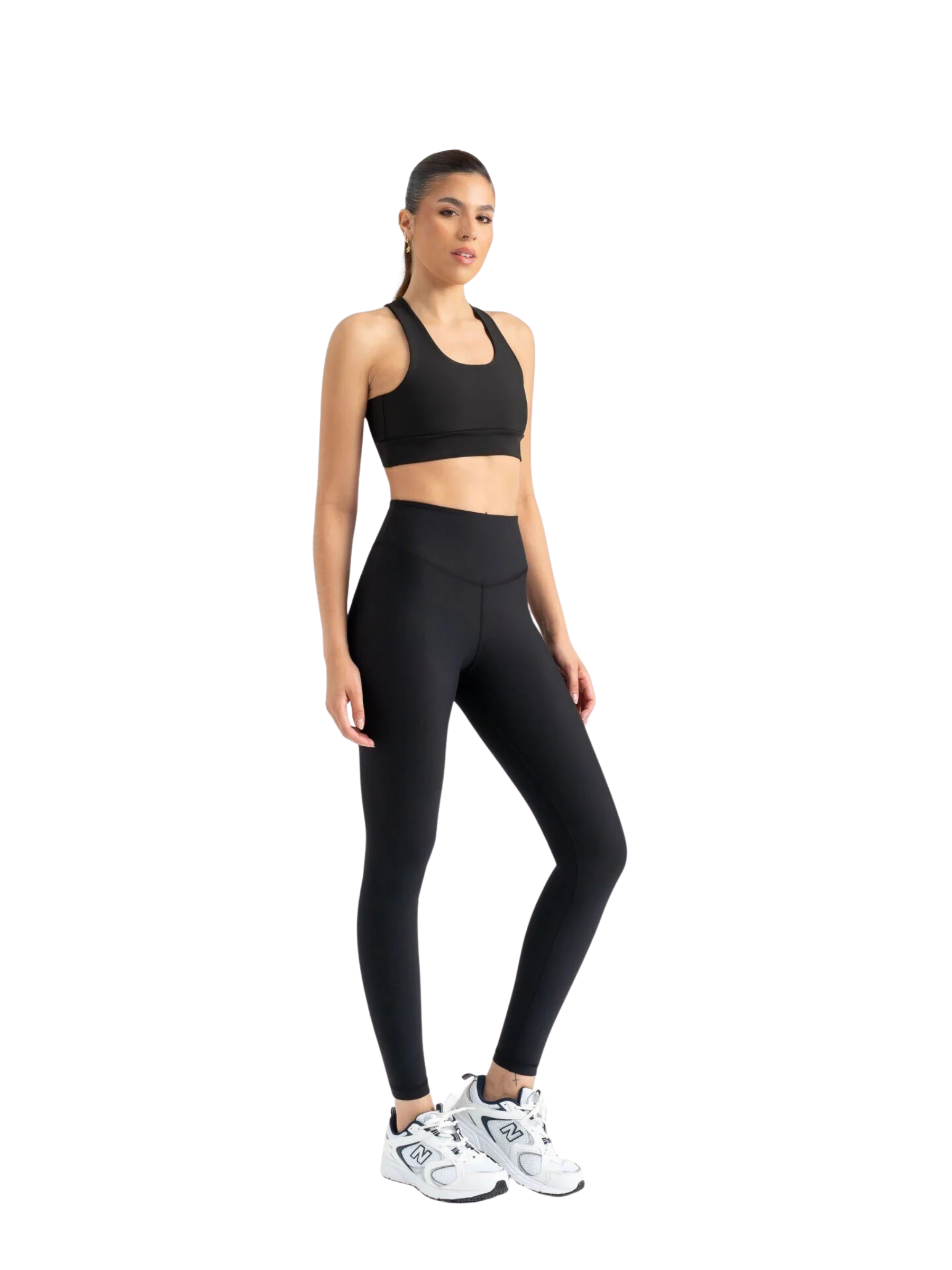 Frau trägt Lismina 408 extra dünne Leggings in Schwarz und Sport-BH, dazu weiße Sneaker vor weißem Hintergrund.