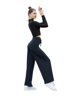 Eine Person posiert mit erhobenem Arm und trägt eine Lismina 359 Mumbai Yoga Hose in Schwarz, schwarze Sportkleidung und weiße Turnschuhe.