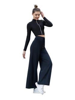 Frau in Lisminas 359 Mumbai Yoga Hose in Schwarz und mit weißen Turnschuhen steht vor einem weißen Hintergrund.
