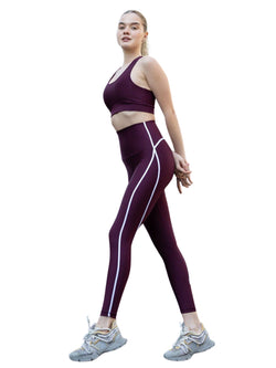 Person in Lisminas 373 Menton Leggings in Dunkelviolett und Sneakers, die sich auf weißem Hintergrund dehnt.