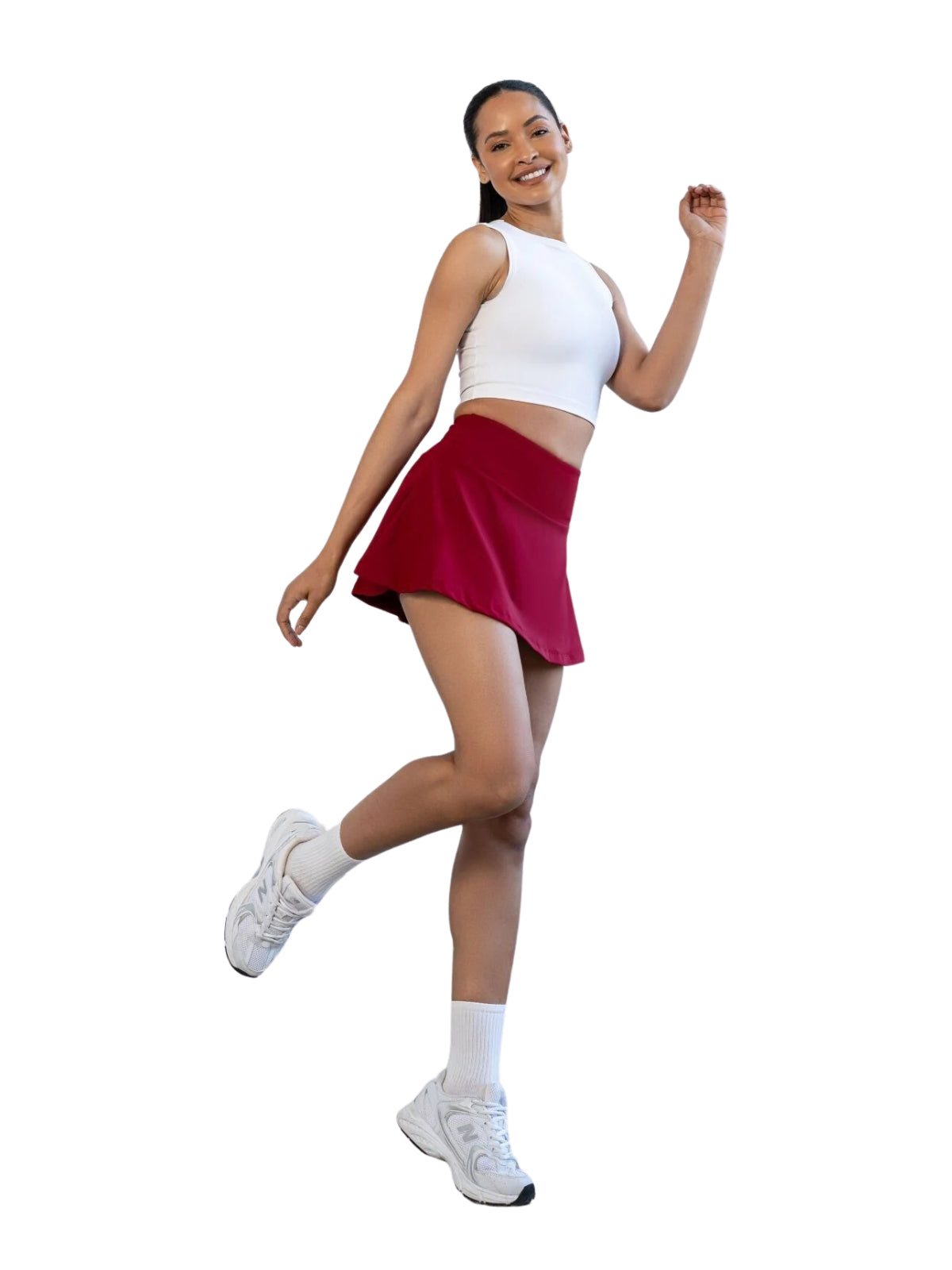 Frau in weißem Crop Top, Lismina 484 Rock in Bordeaux und Turnschuhen, die verspielt auf einem Bein posiert.