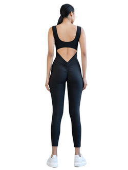 Person, die Lisminas 1400 Scrunch Butt Jumpsuit in Schwarz mit weißen Turnschuhen trägt und mit dem Rücken zur Kamera schaut.