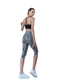 Frau in Lismina 941 Schwarz & Weiss Capri-Leggings, schwarzem Sport-BH, weißen Turnschuhen, Blick nach hinten über die Schulter.