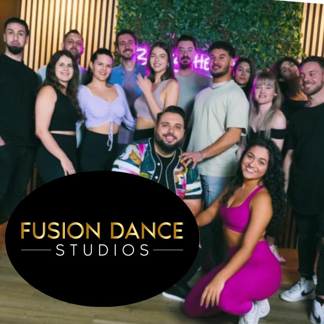 Tanzgruppe posiert in farbenfrohen Outfits mit dem Logo „Fusion Dance Studios“.