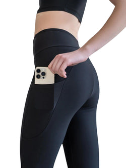 Person in 432 Pocket Schlagleggings von Lismina in Schwarz, die ein Telefon in der praktischen Seitentasche verstaut.