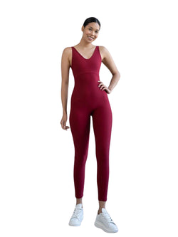 Lächelnde Person in Lisminas 2101 Double Cross Jumpsuit in Bordeaux und weißen Sneakers vor weißem Hintergrund.