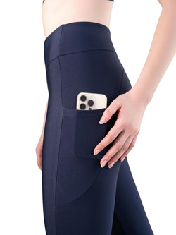 Eine Person in Lisminas 435 Pocket Schlagleggings in Navyblau, mit einem Smartphone sicher in der Seitentasche.