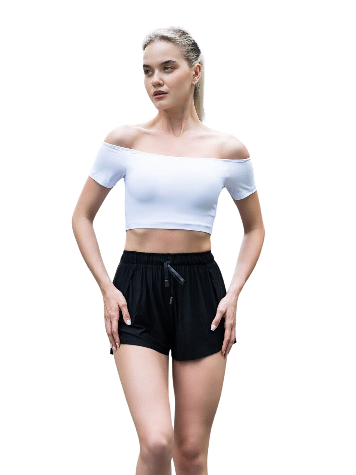 Person, die ein weißes schulterfreies bauchfreies Top und schwarze Shorts trägt und vor einem schlichten weißen Hintergrund steht.