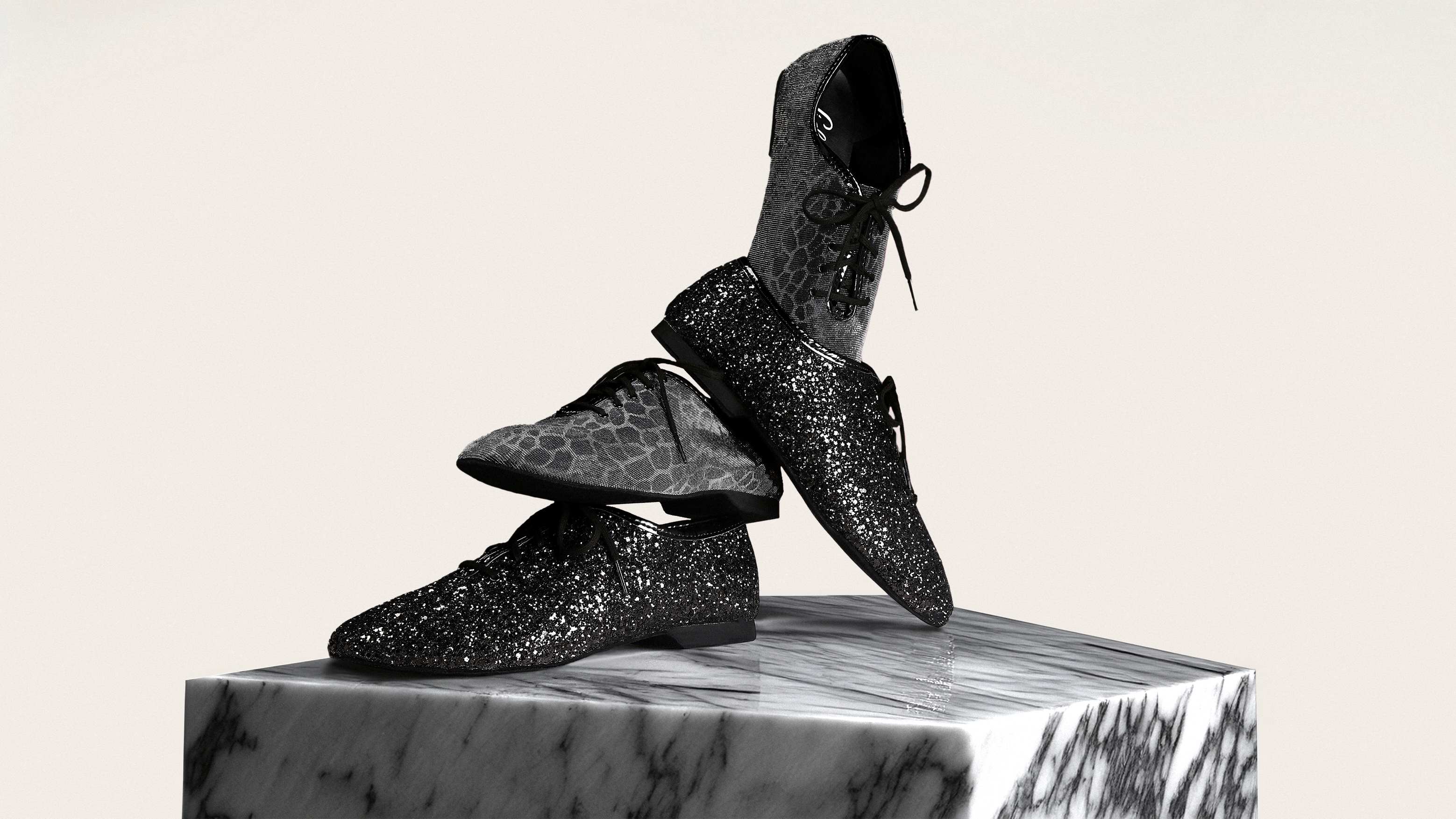 Drei funkelnde Schuhe mit schwarzem und silbernem Muster, gestapelt auf einem Marmorsockel.