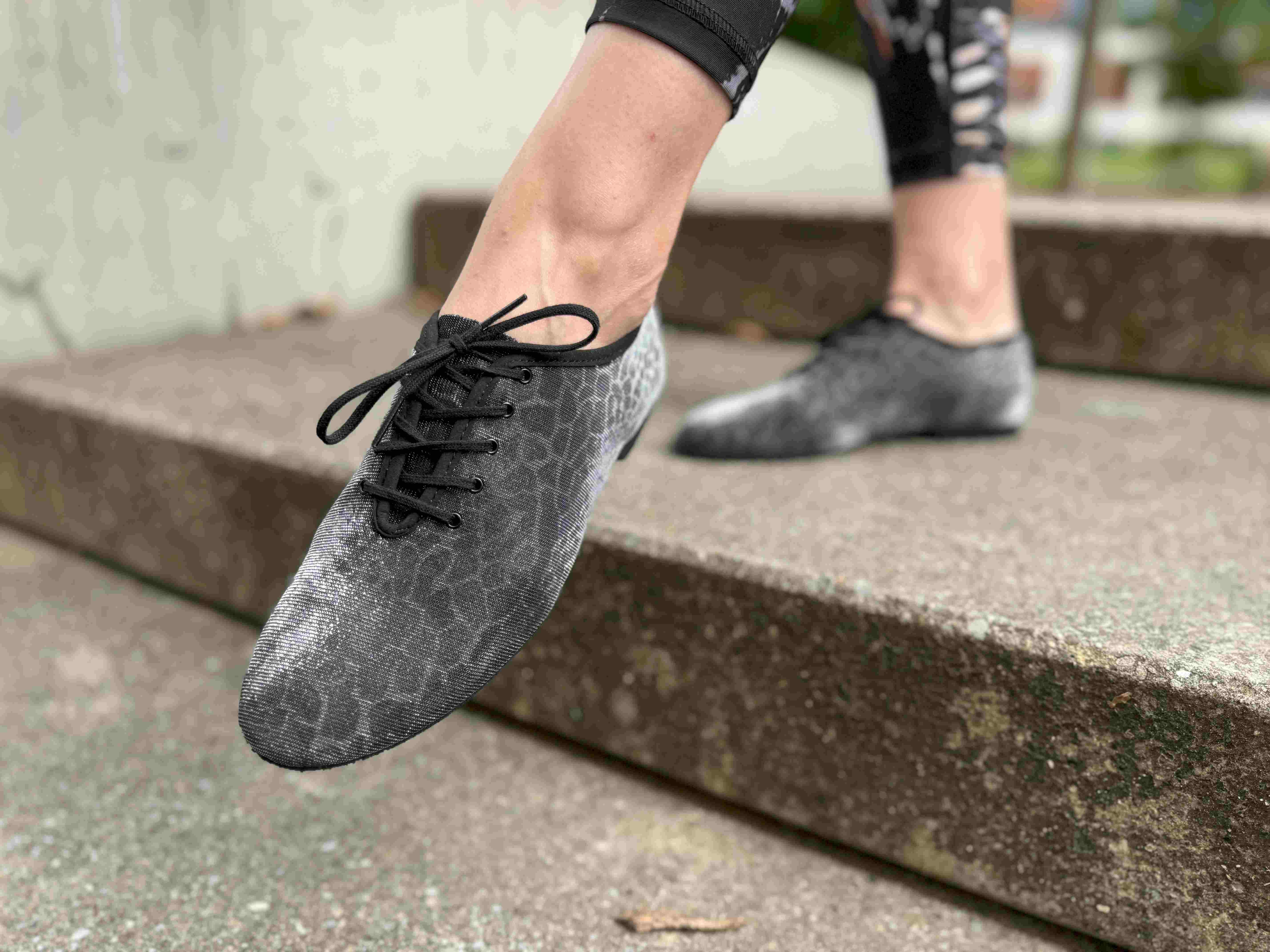 Nahaufnahme einer Person, die schwarze Schnürschuhe mit Strukturmuster trägt und auf Betonstufen tritt.