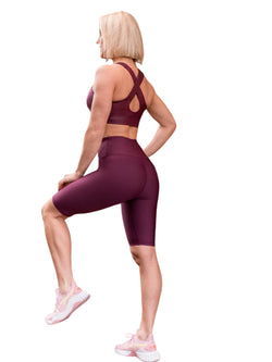 Person in Lisminas kastanienbraunen 6021 Biker-Leggings Ve Waist, Turnschuhen, tritt mit angehobenem Knie nach links und blickt nach links.