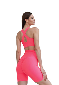 Person in Lisminas 8004 Scrunch Butt Short in Neonpink und überkreuztem Oberteil, steht vor einem weißen Hintergrund.