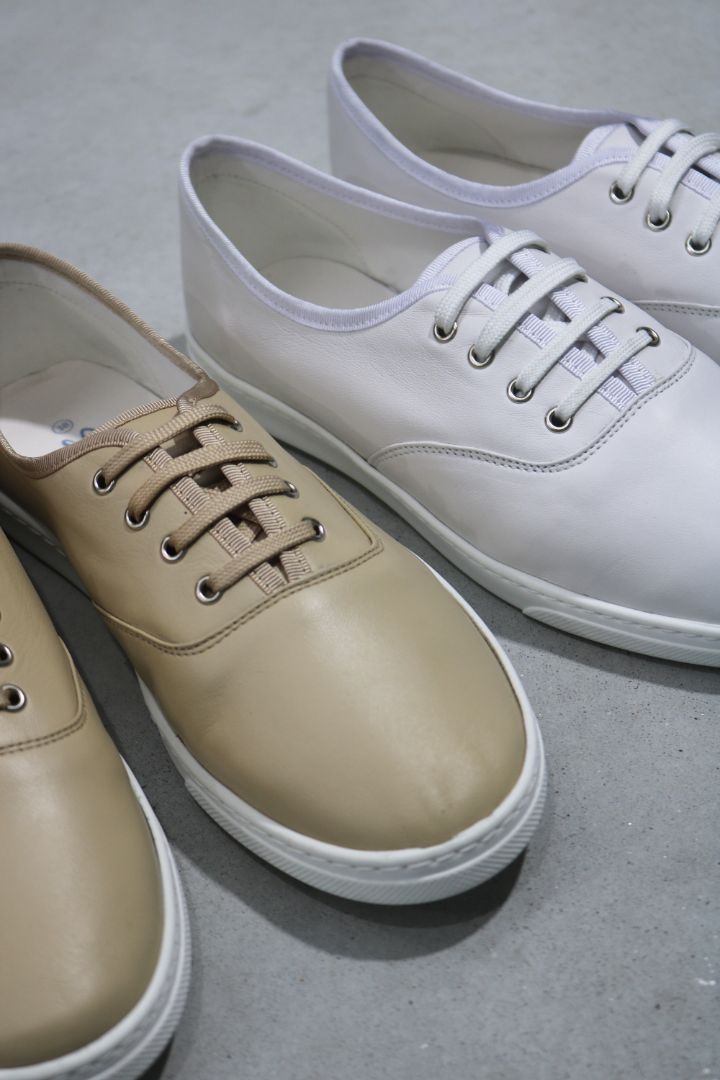 Drei Paar Turnschuhe: hellbraun, weiß und grau, auf hellgrauem Untergrund.