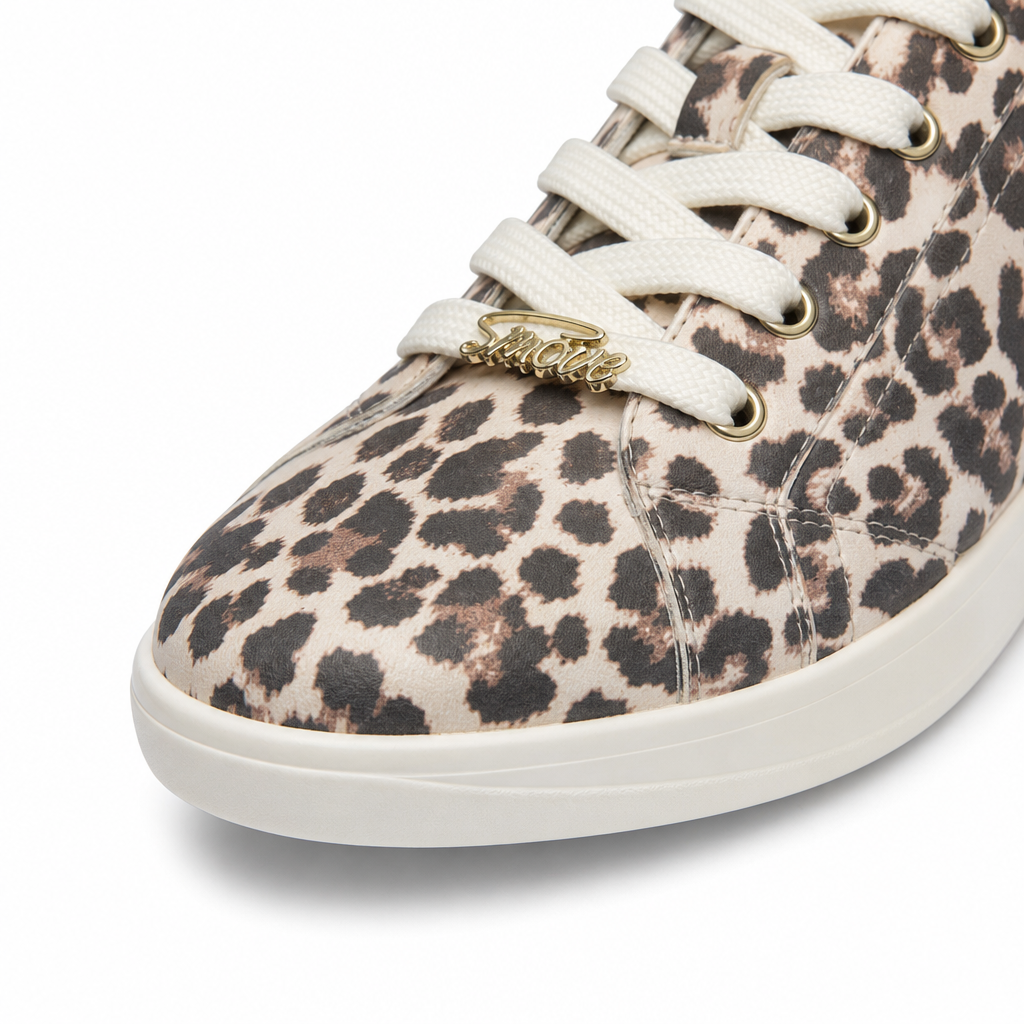 Nahaufnahme des „Dancing Queens SMOVE Accent Dance Sneaker“ in der Farbe „Leo“ für Damen mit weißen Schnürsenkeln und einem goldenen „Smile“-Anhänger.