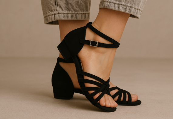 Eine Person, die schwarze Riemchensandalen mit niedrigem Absatz und helle, hochgekrempelte Jeans trägt.