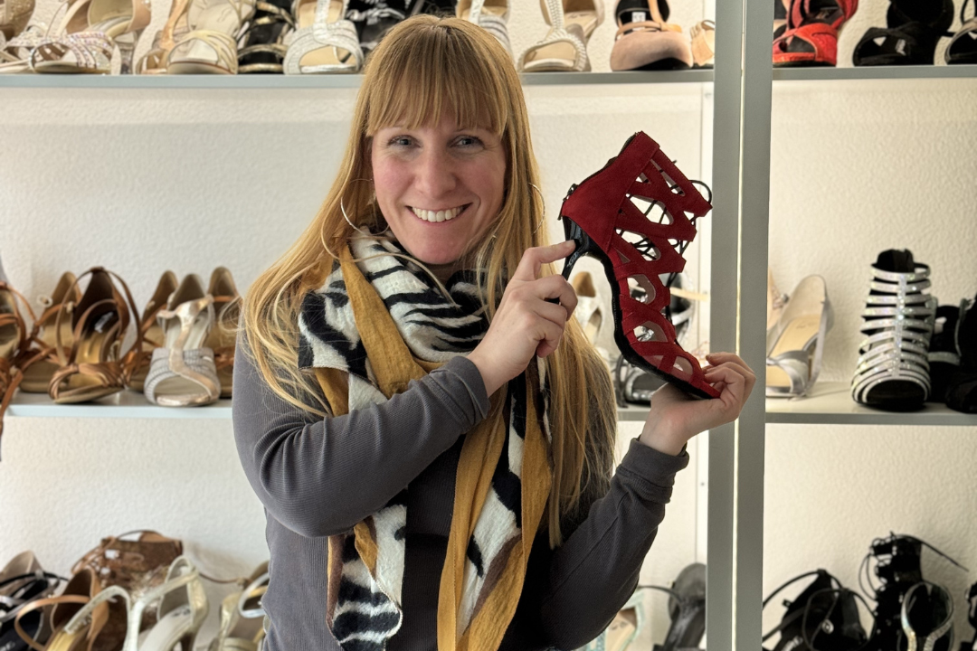 Eine Frau hält einen roten Stöckelschuh vor Regalen voller verschiedener Schuhe.