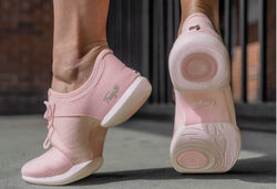 Rosa Turnschuhe mit weißen Sohlen, die von einer Person getragen werden, wobei ein Fuß auf einer Betonoberfläche angehoben ist und das Sohlendesign sichtbar ist.