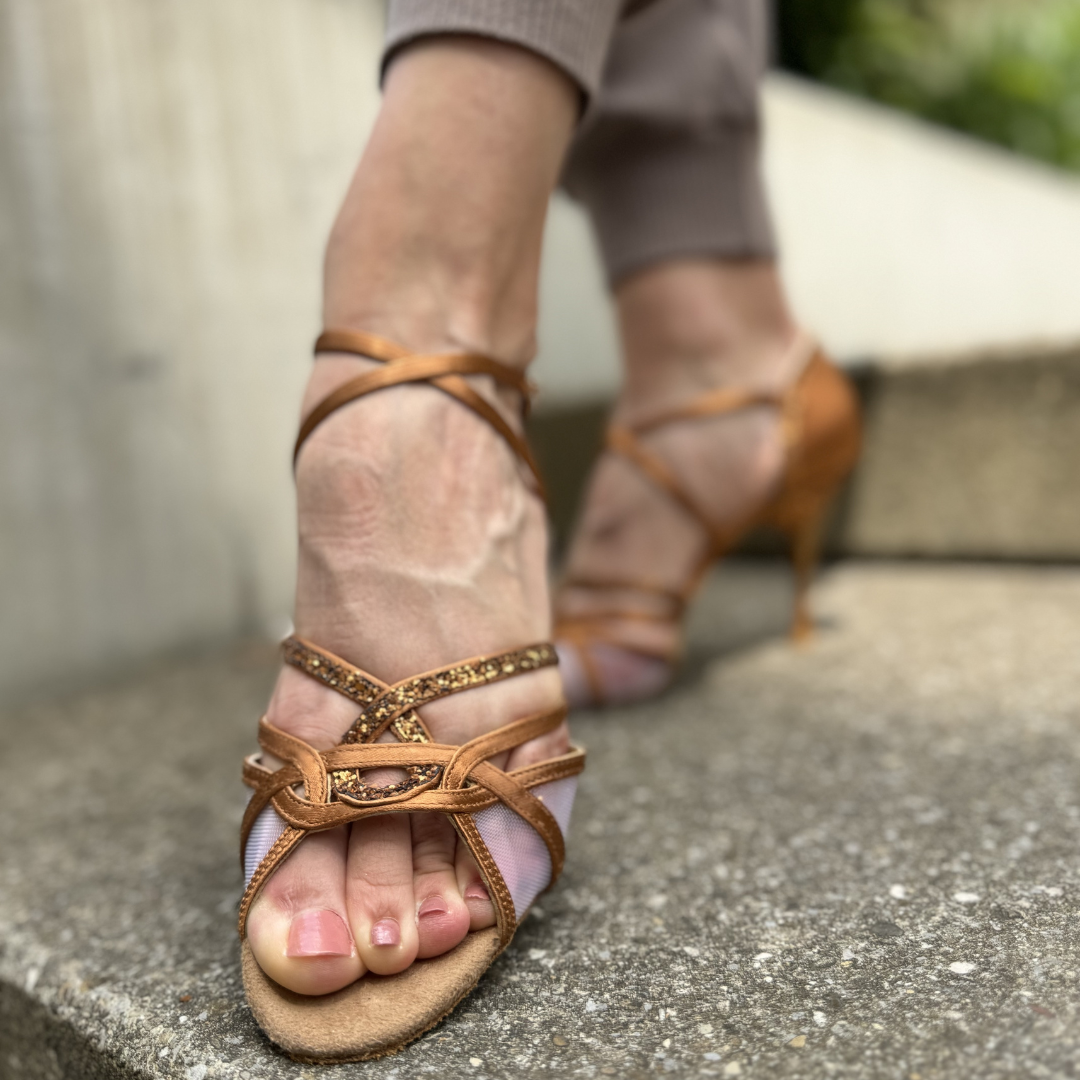 Nahaufnahme einer Person in Portdance PD800 Net Tanzschuhen in Bronze Dark Satin auf einer Betonstufe.