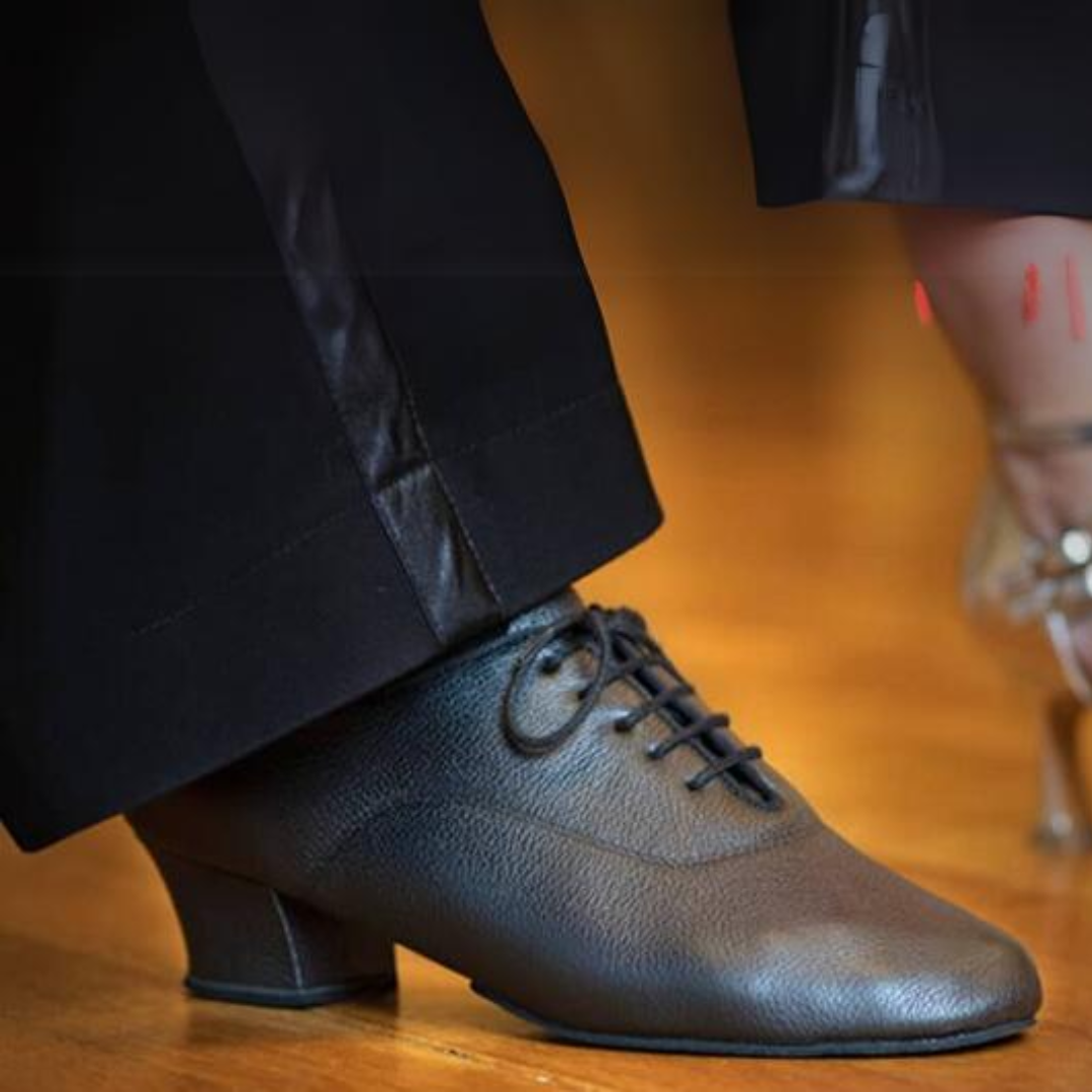 Nahaufnahme von zwei tanzenden Personen. Zu sehen sind polierte Lederschuhe und elegante Schuhe mit Absätzen auf einem Holzboden.