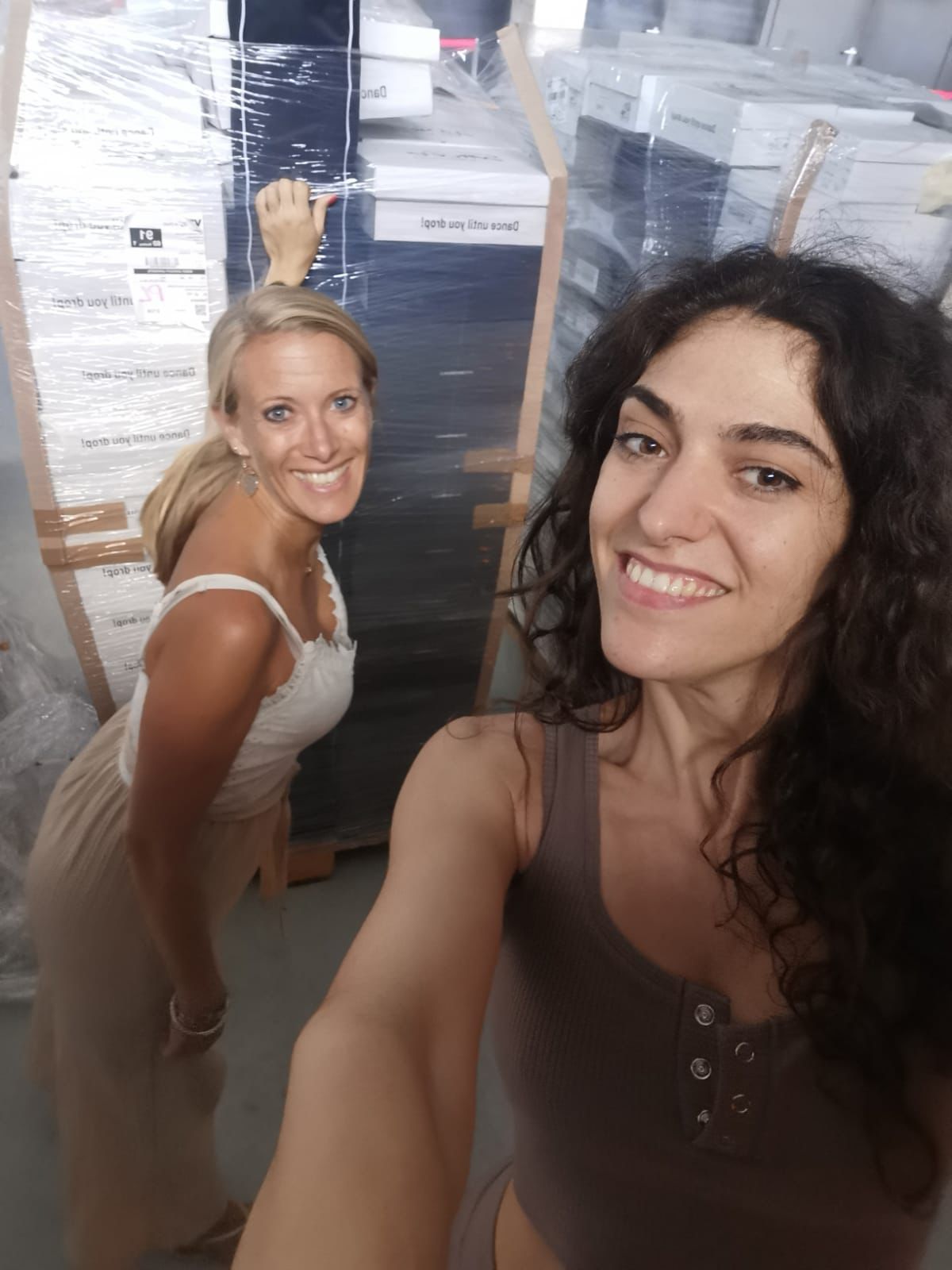 Zwei lächelnde Frauen stehen vor verpackten Paletten in einem Lagerhaus.