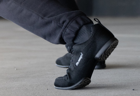 Person in schwarzen Turnschuhen und Hosen, die sich auf einer grauen Oberfläche streckt.