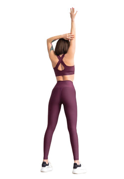 Eine Person streckt sich mit erhobenen Armen und trägt Lisminas 255 High Waist Leggings in Dunkelviolett auf weißem Hintergrund.