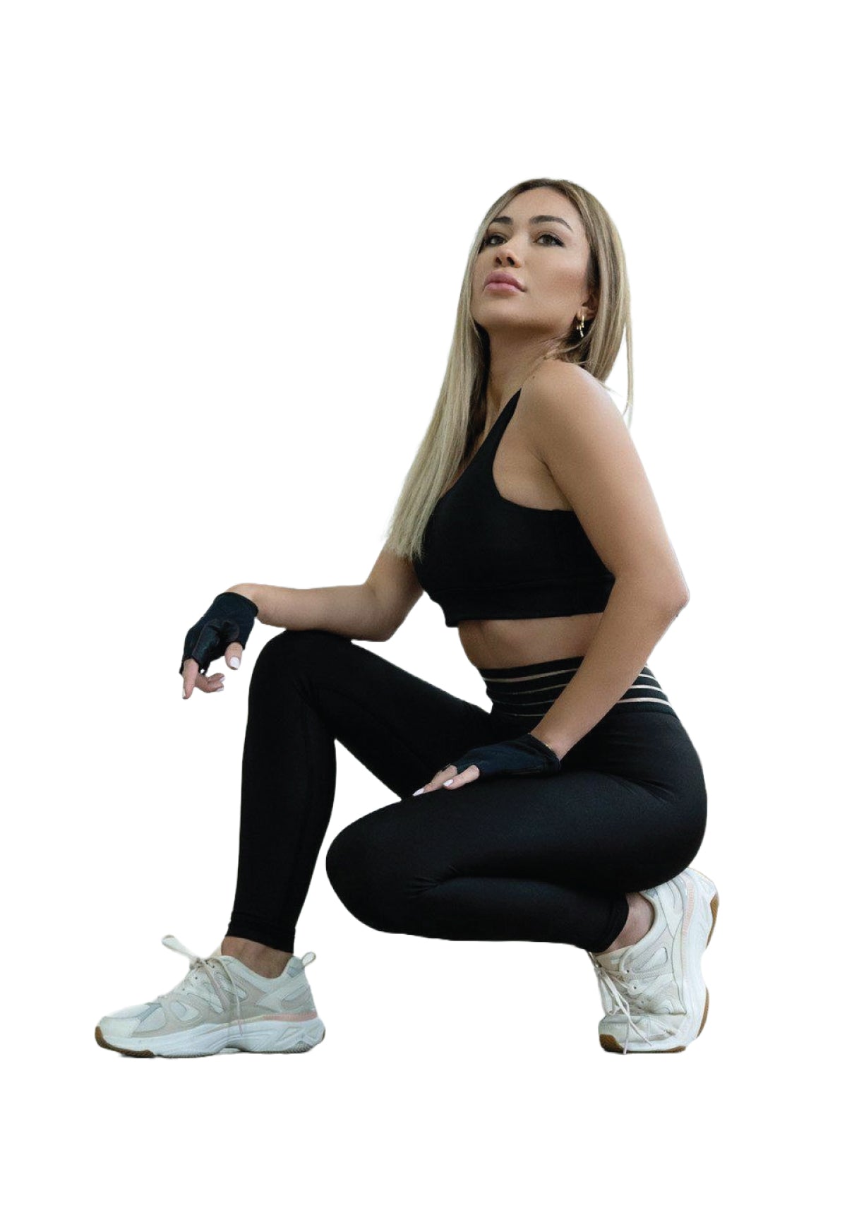 Frau in Lismina 1155 Extra High Waist Leggings in Schwarz und Turnschuhen, kniet auf einem Knie vor einem weißen Hintergrund.