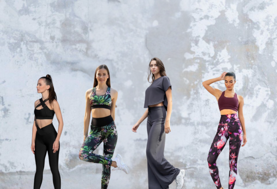 Vier Frauen in Sportkleidung posieren vor einer strukturierten, hellgrauen Wand.
