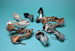 Eine Kollektion funkelnder Stöckelschuhe in Silber, Bronze und Schwarz, angeordnet auf einem blaugrünen Hintergrund.