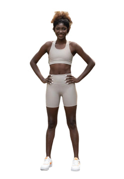 Die Person im Lismina 209 Single Crossed Sport Bra in Beige steht selbstbewusst da, die Hände in die Hüften gestemmt, weiße Sneakers runden den Look ab.