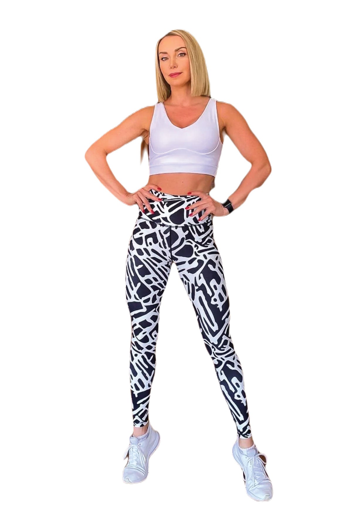 Eine selbstbewusste Frau trägt Lisminas 906 Extra High Waist Leggings in Schwarz & Weiss und einen weißen BH mit weißen Sneakers.