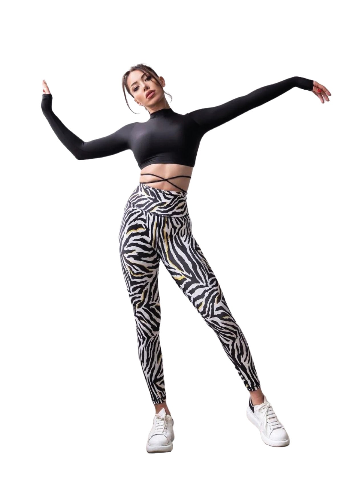 Frau posiert in Lisminas 273 Extra High Waist Leggings in Schwarz & Weiß, einem schwarzen bauchfreien Top und weißen Sneakers.