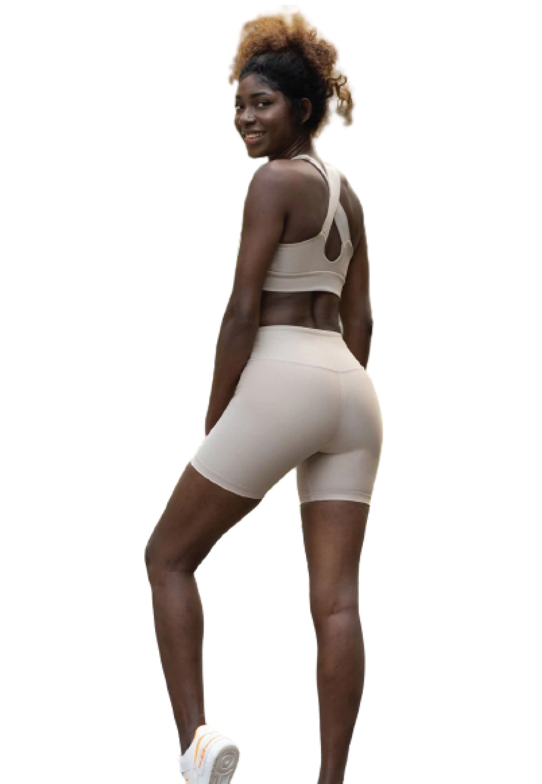 Eine Person in Lisminas beigem 209 Single Crossed Sport Bra lächelt, blickt zurück und balanciert auf einem Bein.