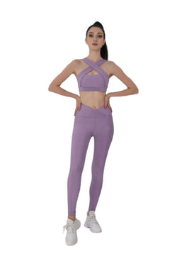 Person in einem Lismina 194 Decoltée Sport-BH in Lila und weißen Turnschuhen, Hände in die Hüften gestemmt, bereit für Yoga.